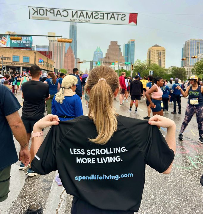 A runner wearing a Less Scrolling. More Living. shirt at the Statesman Cap10K race with the Austin skyline in the background